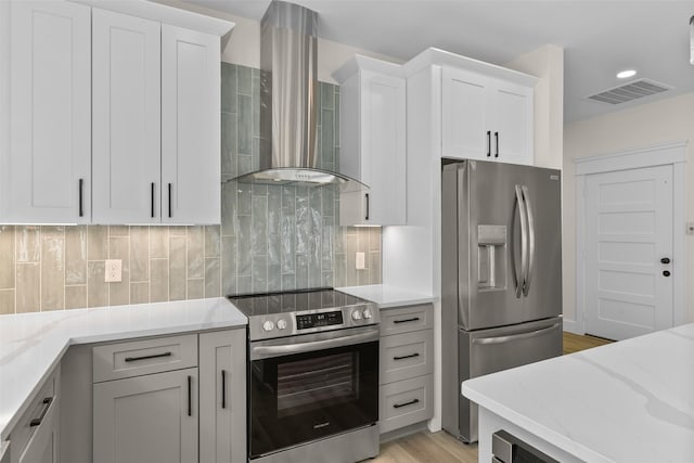 kitchen featuring stainless steel appliances, light stone countertops, wall chimney range hood, and white cabinetry