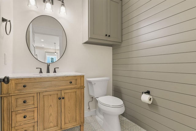 bathroom with toilet, vanity, and wood walls