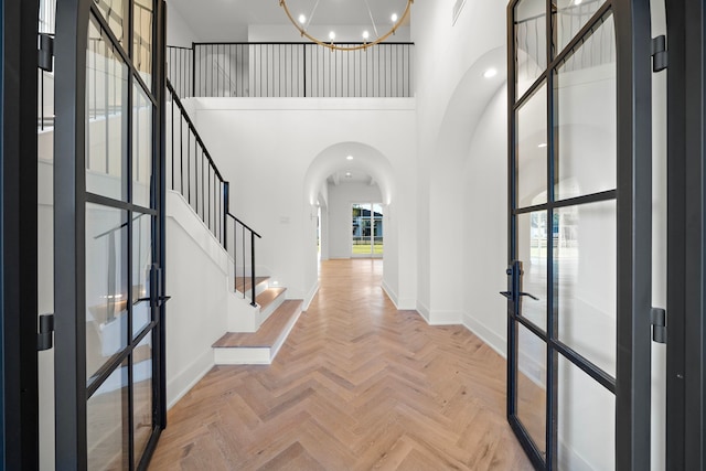 foyer with arched walkways, a notable chandelier, a towering ceiling, baseboards, and french doors