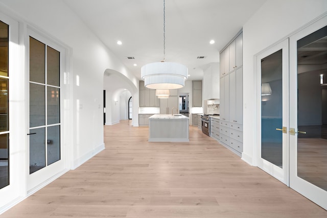 corridor with light wood finished floors, baseboards, arched walkways, a sink, and recessed lighting