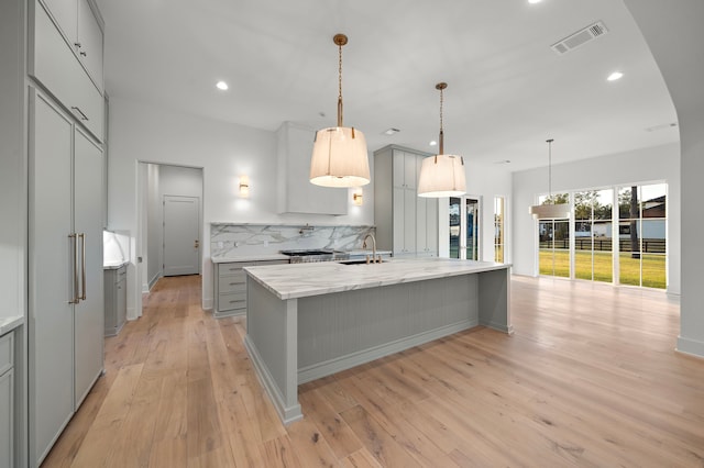 kitchen with visible vents, decorative backsplash, gray cabinetry, light wood-style floors, and a sink