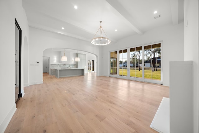 unfurnished living room featuring baseboards, arched walkways, light wood-style flooring, beam ceiling, and recessed lighting