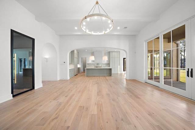 unfurnished living room with baseboards, arched walkways, light wood-style flooring, beam ceiling, and a notable chandelier