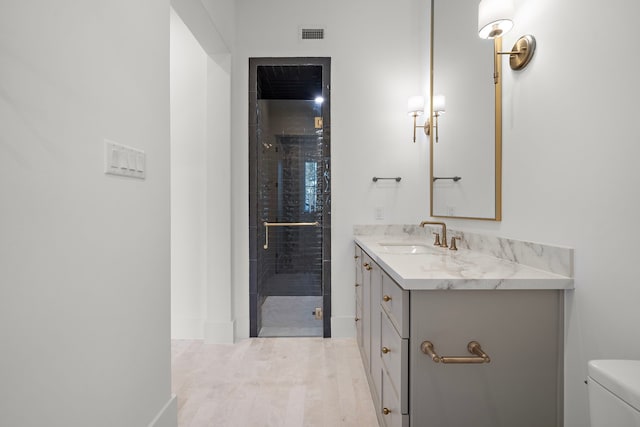 bathroom with visible vents, toilet, vanity, a shower stall, and wood finished floors