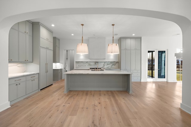 kitchen with light wood finished floors, arched walkways, gray cabinets, and light countertops