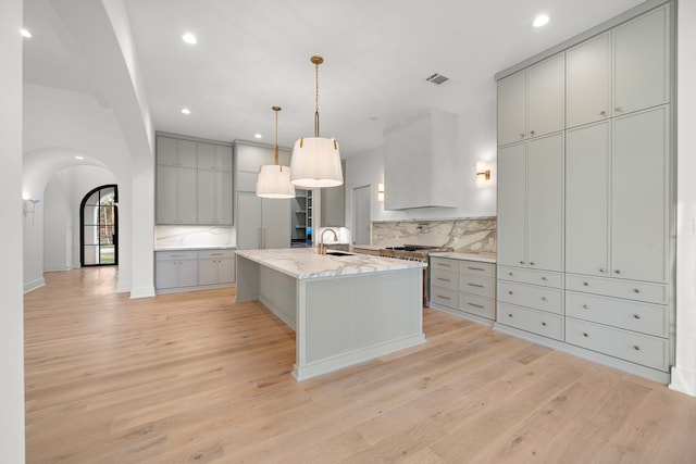 kitchen with tasteful backsplash, arched walkways, gray cabinets, light wood-style floors, and a sink