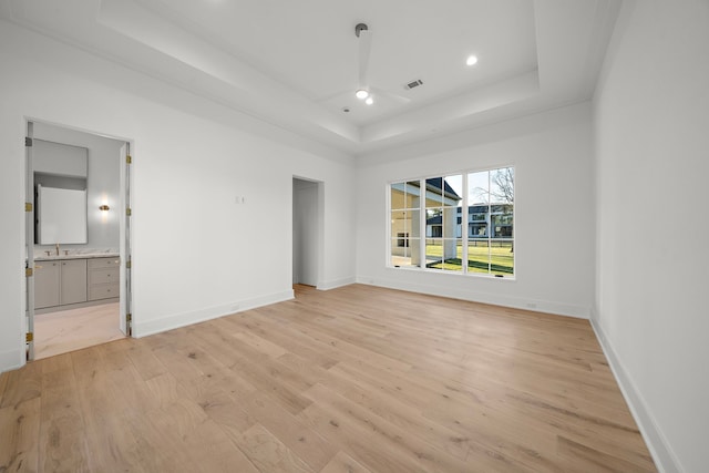 unfurnished bedroom featuring recessed lighting, visible vents, baseboards, light wood-style floors, and a tray ceiling