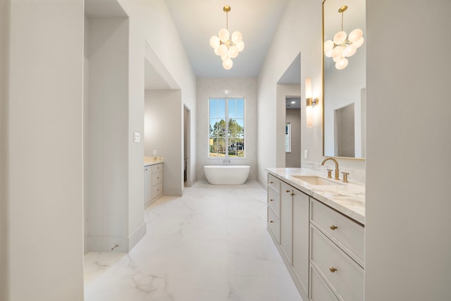 full bath with a chandelier, vanity, baseboards, a freestanding bath, and marble finish floor