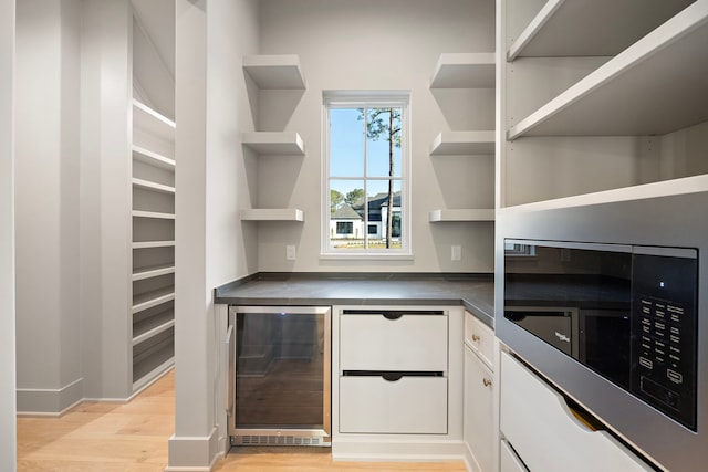 interior space featuring wine cooler, light wood-style flooring, white cabinets, open shelves, and dark countertops