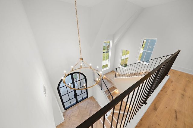 stairway with parquet floors, visible vents, high vaulted ceiling, and a notable chandelier