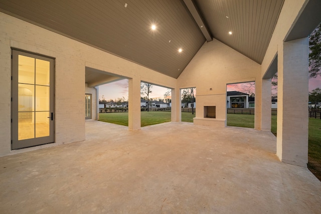 patio terrace at dusk with a yard, exterior fireplace, and fence