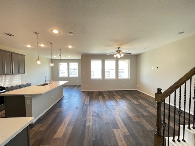 kitchen featuring backsplash, decorative light fixtures, dark hardwood / wood-style floors, an island with sink, and ceiling fan