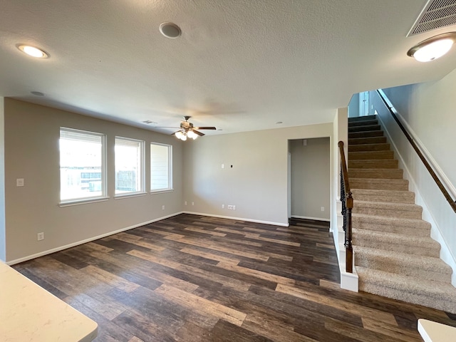 unfurnished living room with a textured ceiling, ceiling fan, and dark wood-type flooring