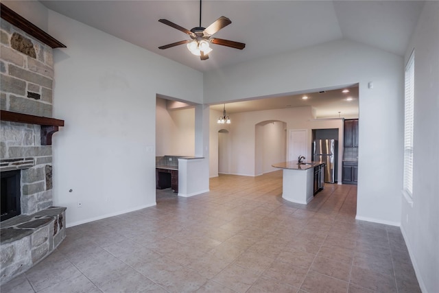 unfurnished living room with ceiling fan, sink, a fireplace, lofted ceiling, and light tile patterned flooring