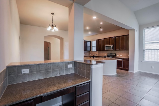 kitchen with vaulted ceiling, decorative backsplash, dark stone countertops, dark brown cabinetry, and stainless steel appliances