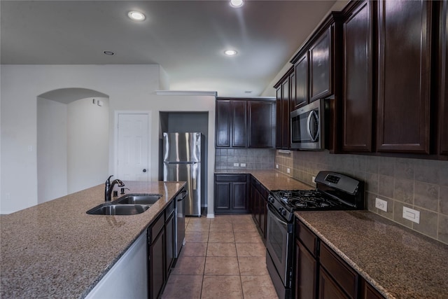 kitchen featuring sink, dark stone countertops, appliances with stainless steel finishes, tasteful backsplash, and dark brown cabinetry