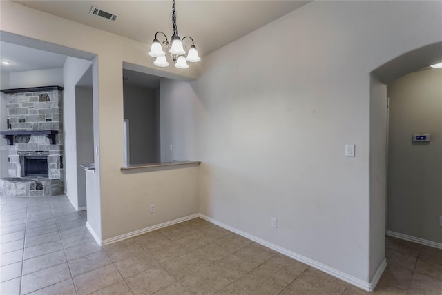 unfurnished dining area with a stone fireplace, light tile patterned floors, and a chandelier