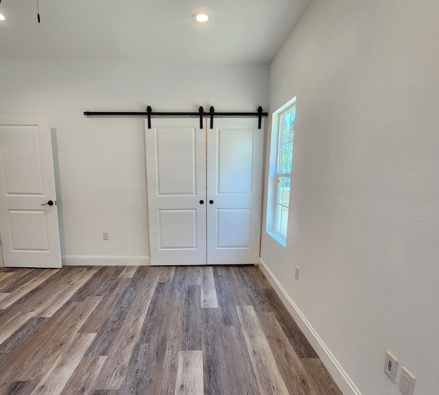 unfurnished bedroom with wood-type flooring, a barn door, and a closet