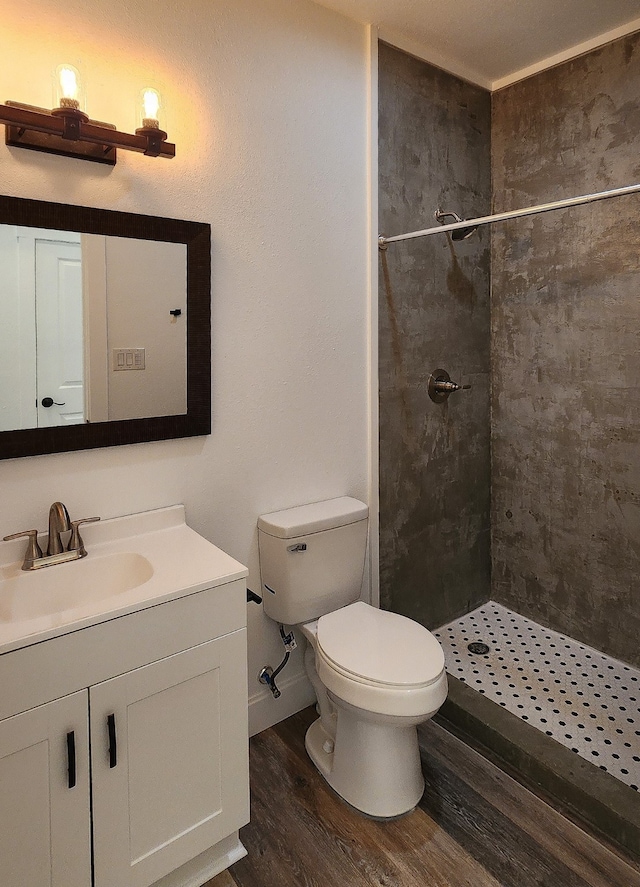 bathroom featuring a tile shower, vanity, wood-type flooring, and toilet