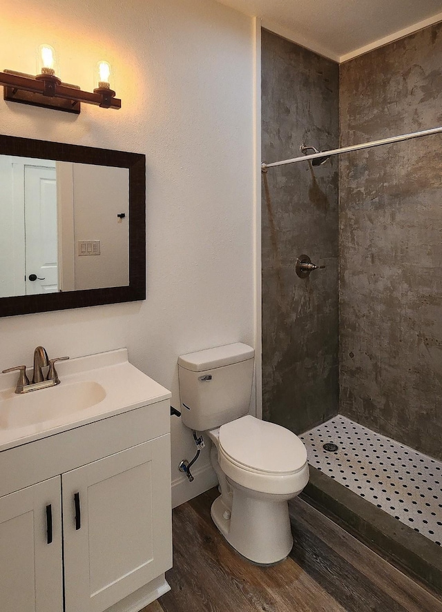 bathroom with a tile shower, hardwood / wood-style flooring, toilet, and vanity