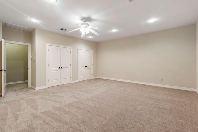 unfurnished bedroom with ceiling fan, light colored carpet, and two closets