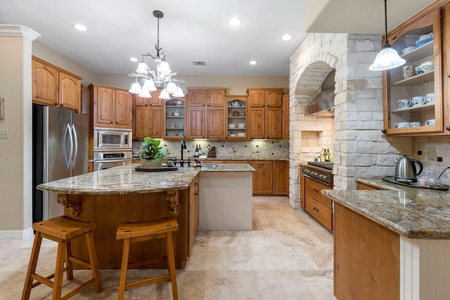 kitchen with light stone countertops, an inviting chandelier, backsplash, a center island with sink, and appliances with stainless steel finishes