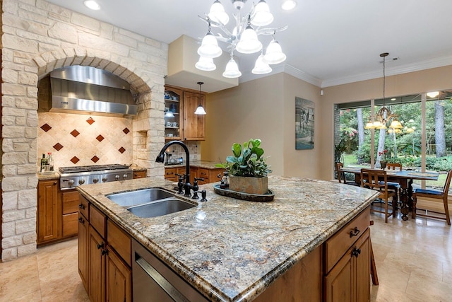 kitchen with tasteful backsplash, wall chimney range hood, sink, a center island with sink, and an inviting chandelier