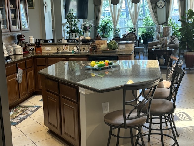 bar featuring dark stone counters, dishwashing machine, sink, and light tile patterned floors