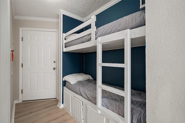 bedroom with a textured ceiling, light wood-type flooring, and ornamental molding