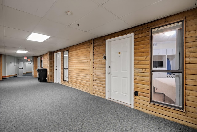 interior space featuring a drop ceiling, carpet floors, and wooden walls