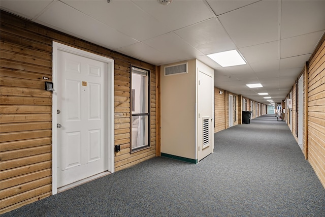 hall featuring carpet flooring, a paneled ceiling, and wood walls