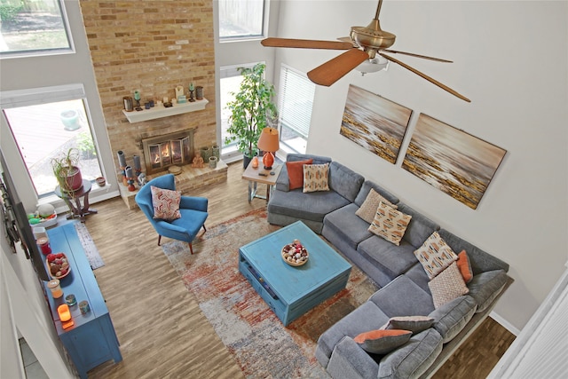 living room with ceiling fan, hardwood / wood-style floors, brick wall, a brick fireplace, and a towering ceiling