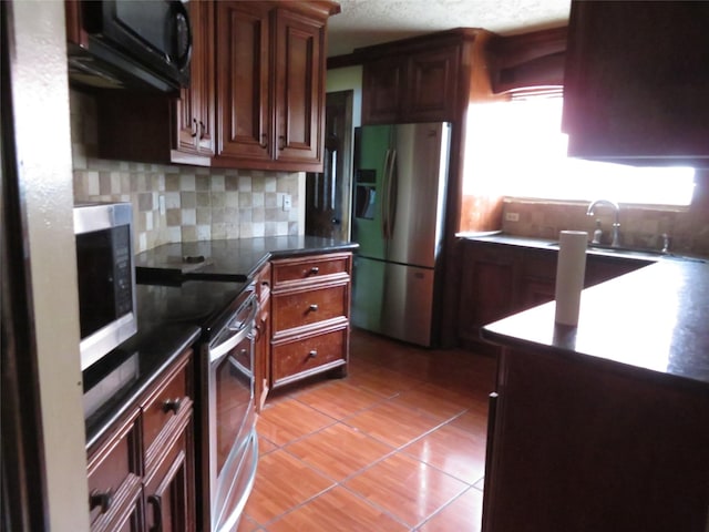 kitchen with stainless steel appliances, light tile patterned floors, backsplash, and dark countertops