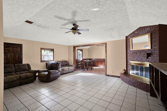 tiled living room featuring lofted ceiling, a fireplace, a textured ceiling, and ceiling fan