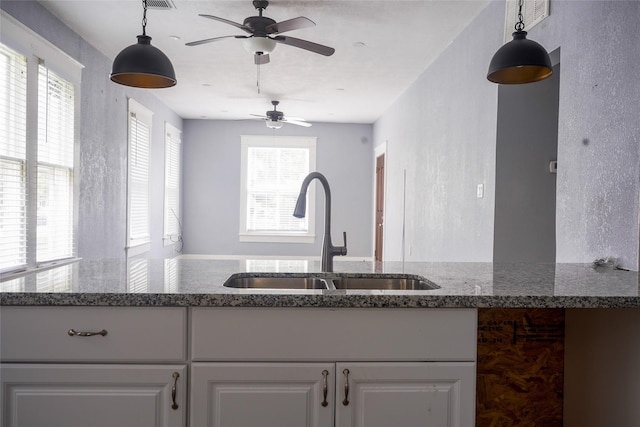 kitchen with dark stone counters, a ceiling fan, pendant lighting, and a sink
