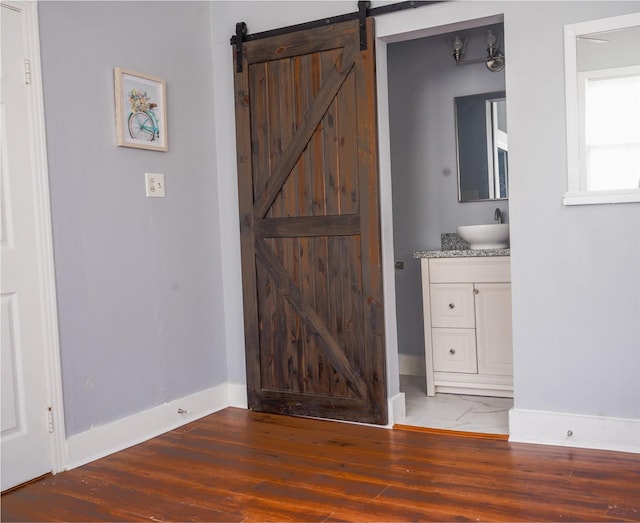 interior space featuring wood finished floors, baseboards, a barn door, connected bathroom, and a sink