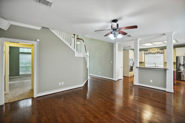 unfurnished living room with sink, ornate columns, dark wood-type flooring, ceiling fan, and ornamental molding