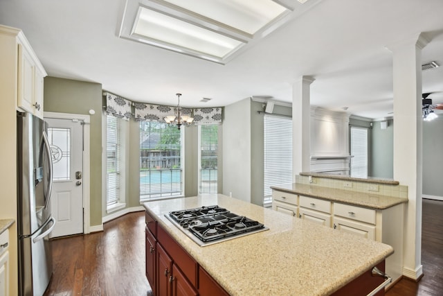 kitchen featuring hanging light fixtures, ceiling fan with notable chandelier, a center island, appliances with stainless steel finishes, and dark wood-type flooring