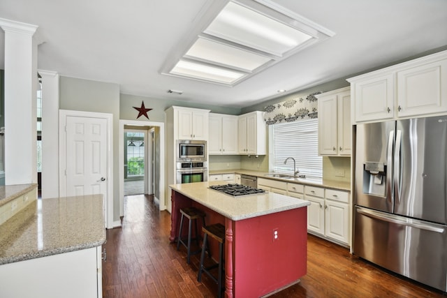 kitchen featuring appliances with stainless steel finishes, sink, white cabinetry, a center island, and dark wood-type flooring