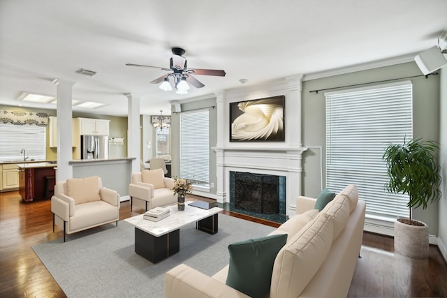 living room featuring decorative columns, ceiling fan with notable chandelier, a fireplace, wood-type flooring, and sink