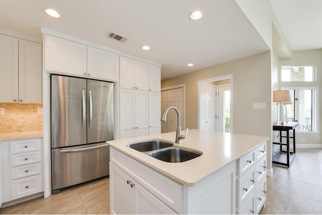 kitchen featuring sink, white cabinets, stainless steel refrigerator, and an island with sink