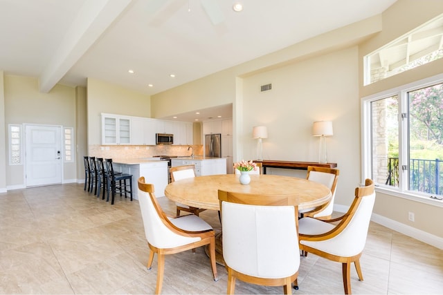 dining space with sink, beam ceiling, light tile patterned floors, and a high ceiling