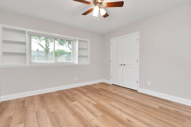 unfurnished room with built in shelves, ceiling fan, and light wood-type flooring