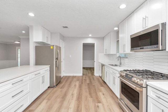 kitchen featuring tasteful backsplash, stainless steel appliances, white cabinets, sink, and light hardwood / wood-style flooring