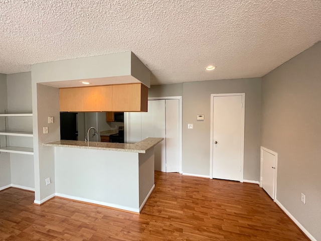 kitchen featuring range, kitchen peninsula, a textured ceiling, light brown cabinetry, and wood-type flooring