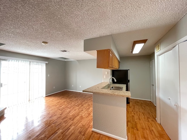 kitchen featuring sink, light hardwood / wood-style flooring, a textured ceiling, kitchen peninsula, and a kitchen breakfast bar