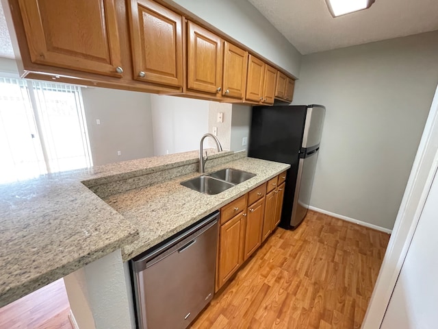 kitchen featuring sink, appliances with stainless steel finishes, light hardwood / wood-style flooring, and light stone counters