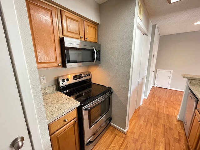 kitchen with light hardwood / wood-style floors, light stone counters, appliances with stainless steel finishes, and a textured ceiling