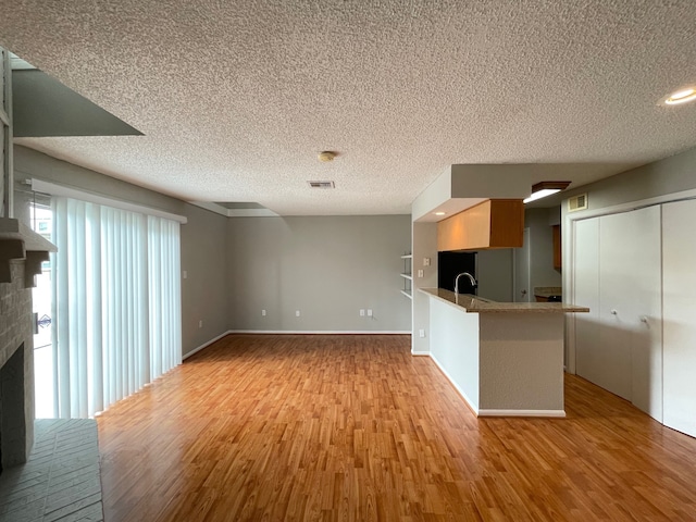 kitchen with a breakfast bar area, a brick fireplace, kitchen peninsula, and light wood-type flooring