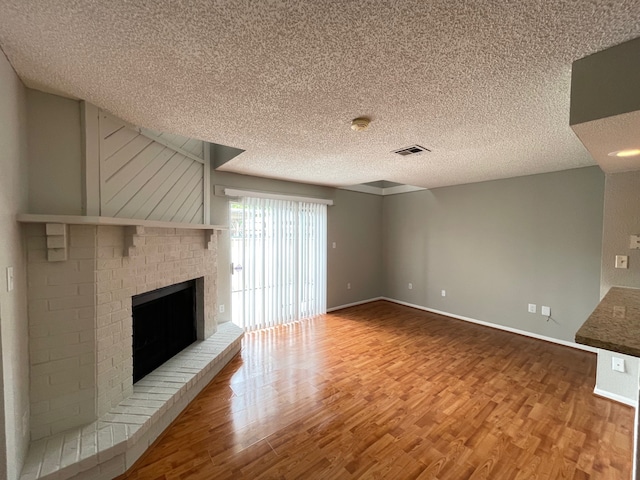 unfurnished living room with a textured ceiling, wood-type flooring, and a brick fireplace